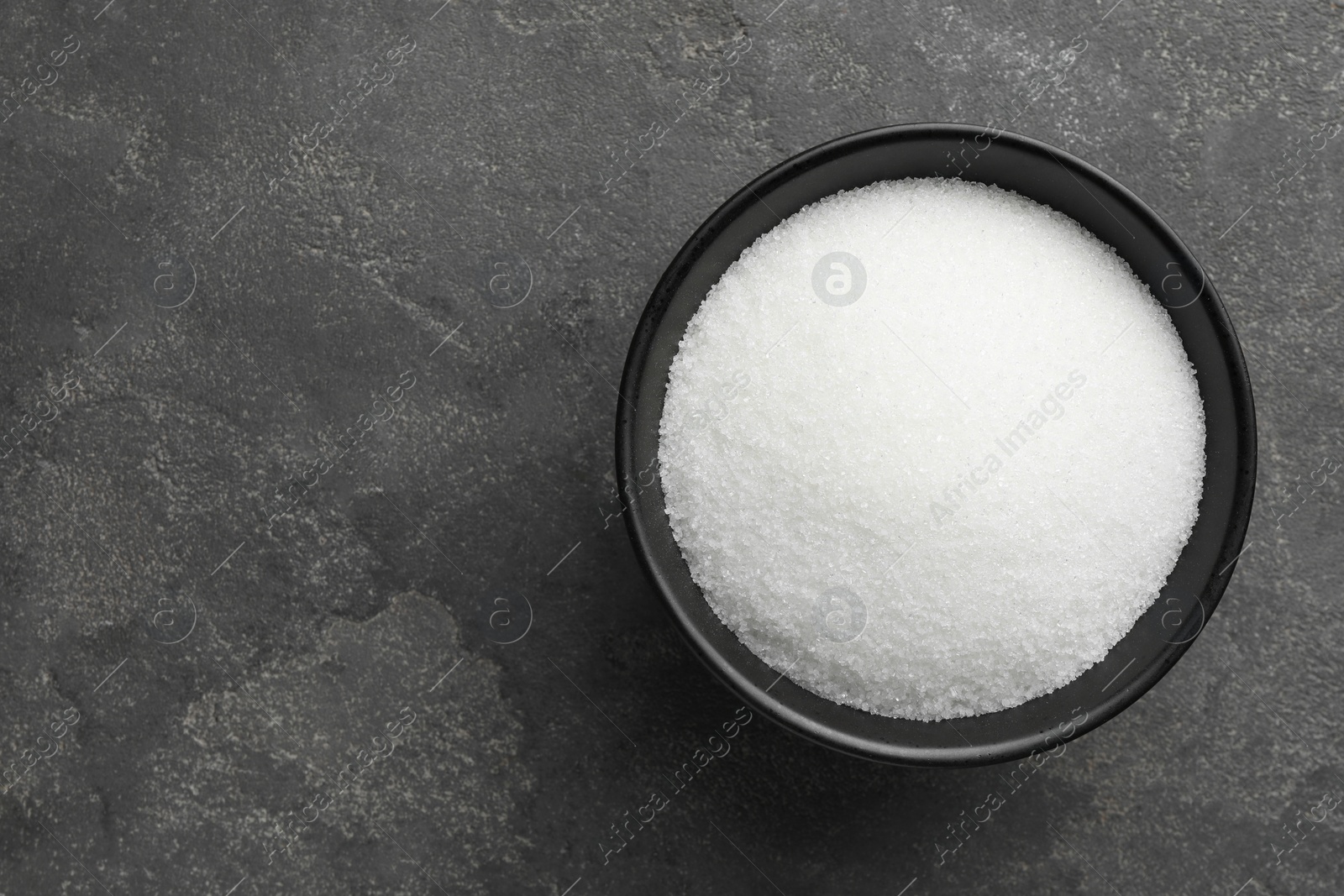 Photo of Granulated sugar in bowl on grey textured table, top view. Space for text