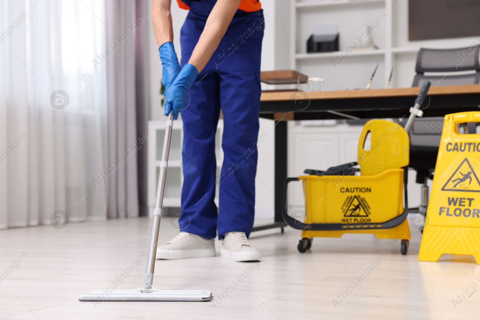 Photo of Cleaning service worker washing floor with mop, closeup. Bucket with wet floor sign in office