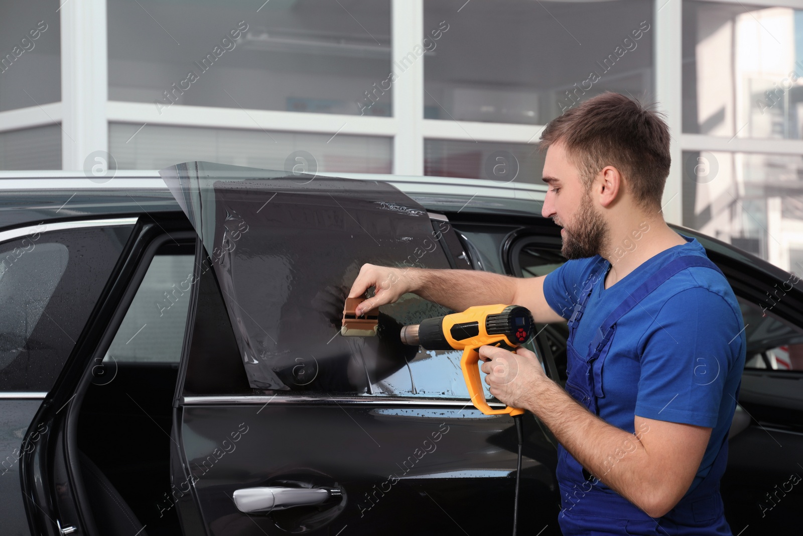 Photo of Worker tinting car window with heat gun in workshop