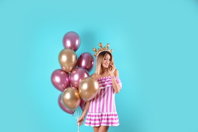 Young woman with crown and air balloons on color background