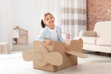 Photo of Cute little girl playing with cardboard airplane in living room