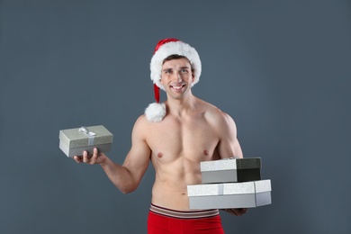 Photo of Young muscular man in Santa hat with gift boxes on gray background