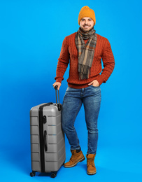 Photo of Young man in warm clothes with suitcase on blue background. Winter vacation