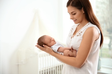 Young woman holding her newborn baby at home. Space for text