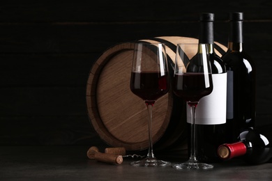 Composition with glasses and bottles of red wine on table against dark background. Space for text