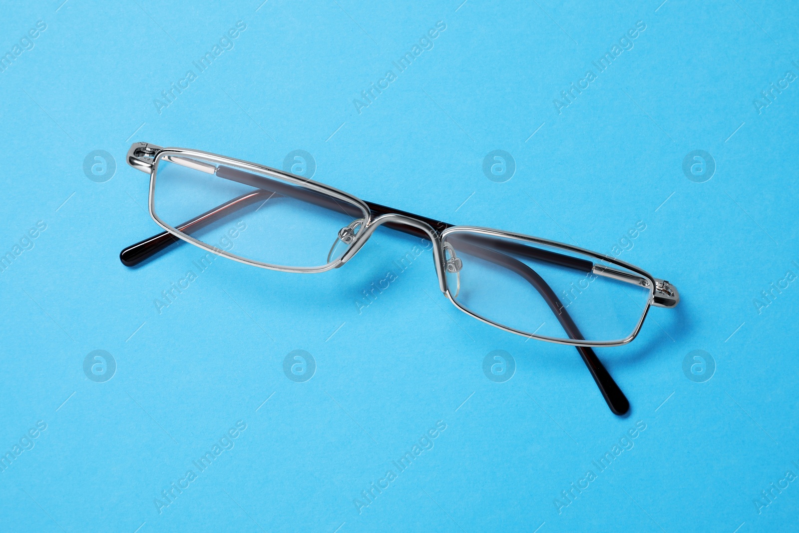 Photo of Glasses in stylish frame on light blue background, top view