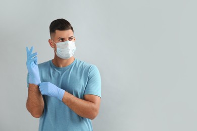 Photo of Man in protective face mask putting on medical gloves against grey background. Space for text