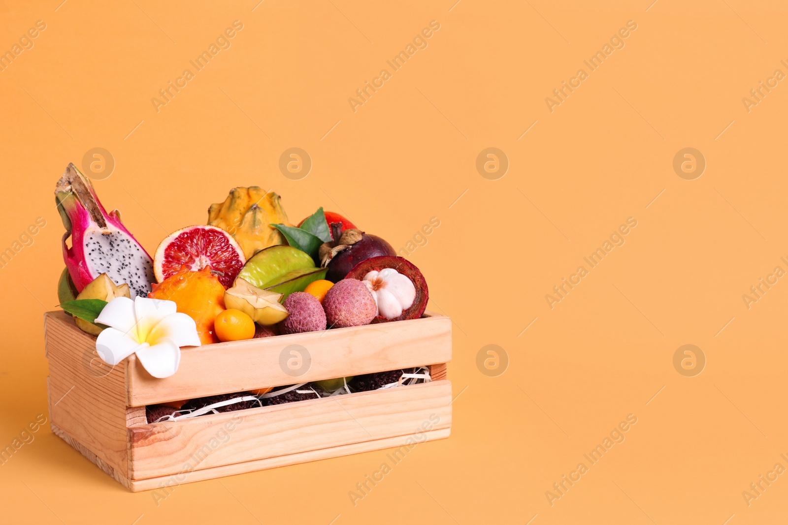 Photo of Different tropical fruits in wooden box on yellow background. Space for text