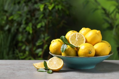 Fresh lemons and green leaves on grey table outdoors. Space for text