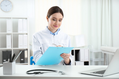 Photo of Young female doctor working at table in office