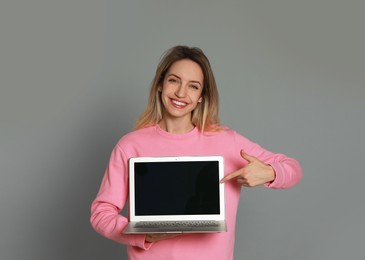 Photo of Young woman with modern laptop on grey background