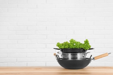 Photo of Stack of clean cookware with lettuce on table against white brick wall. Space for text