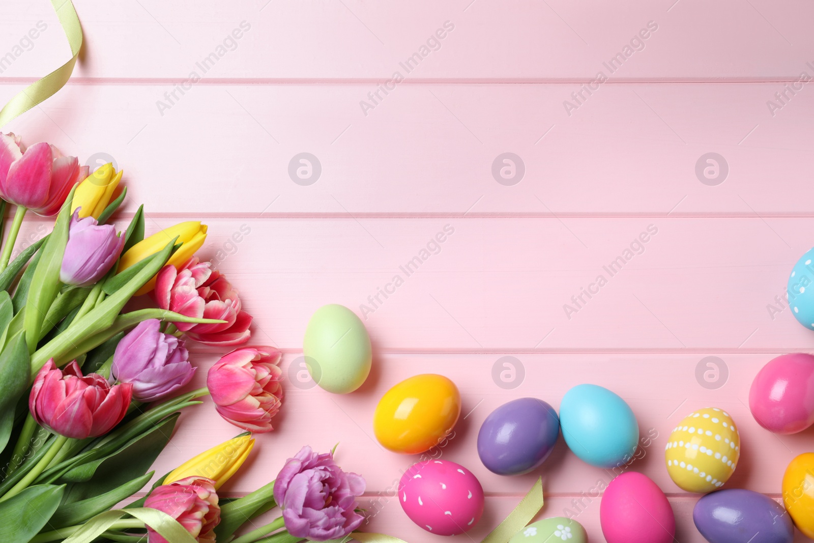 Photo of Bright painted eggs and spring tulips on pink wooden table, flat lay with space for text. Happy Easter