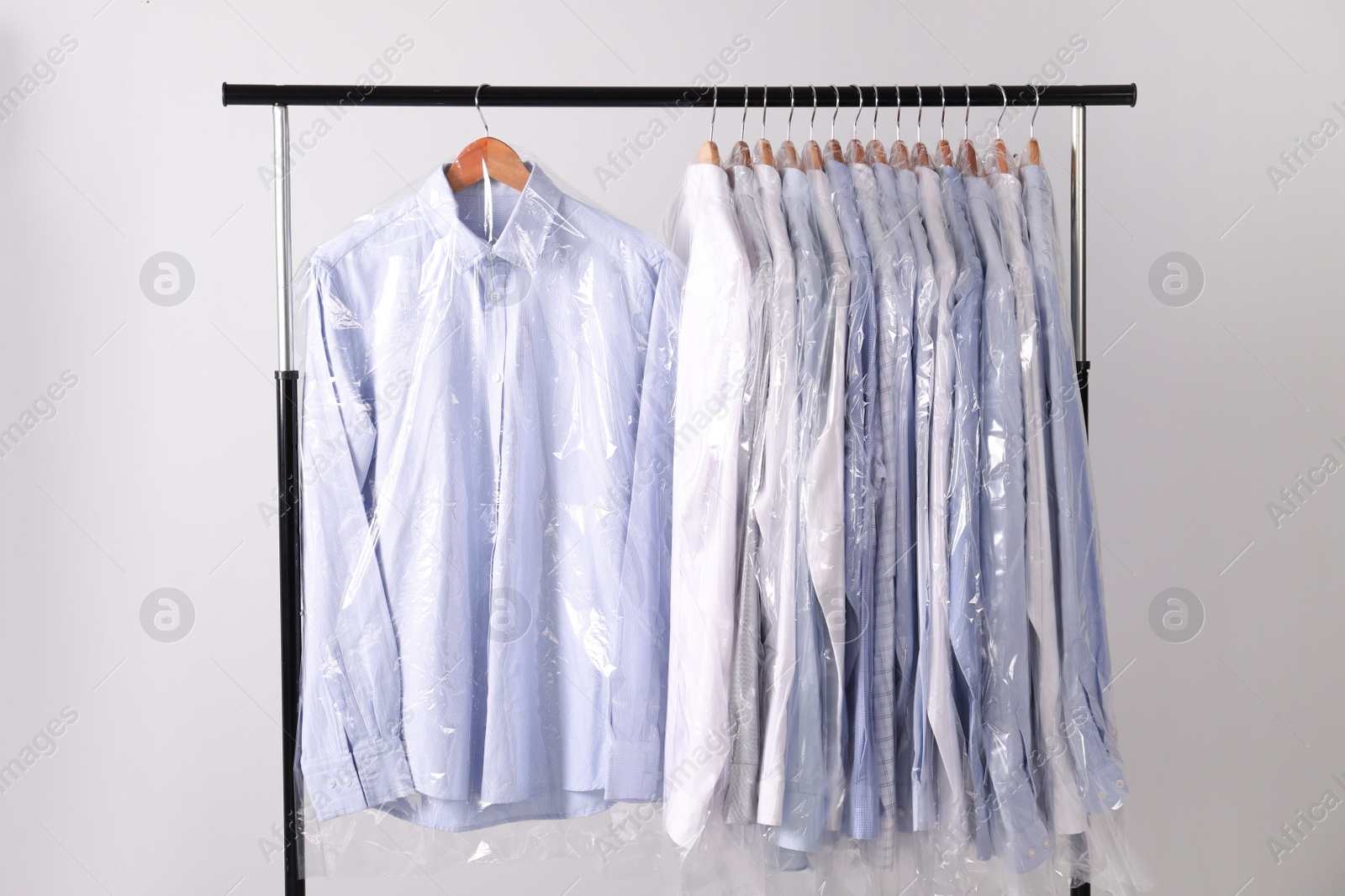 Photo of Hangers with shirts in dry cleaning plastic bags on rack against light background