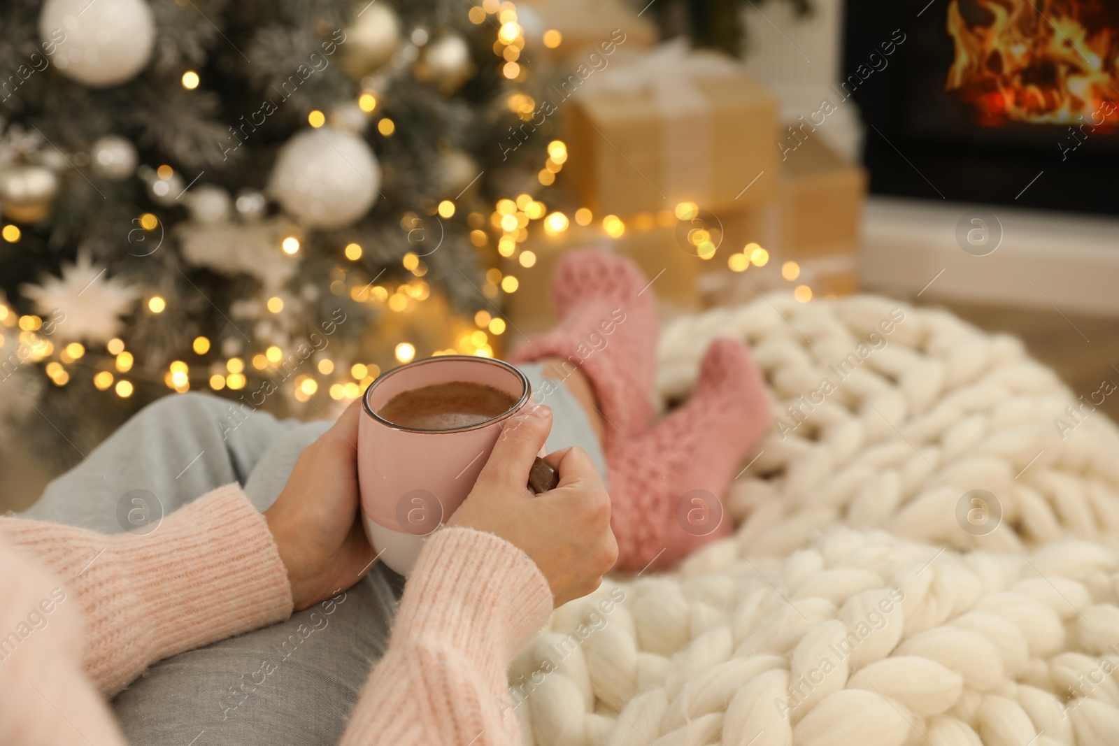 Photo of Woman with cup of hot drink resting near fireplace  in living room decorated for Christmas, closeup
