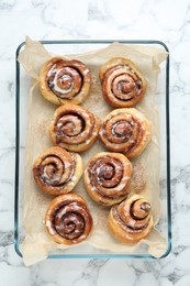 Photo of Baking dish with tasty cinnamon rolls on white marble table, top view