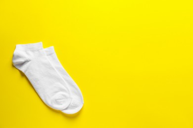 Photo of Pair of white socks on yellow background, flat lay. Space for text