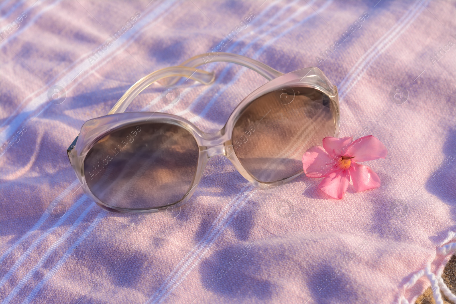 Photo of Beautiful sunglasses with tropical flower on pink blanket, closeup