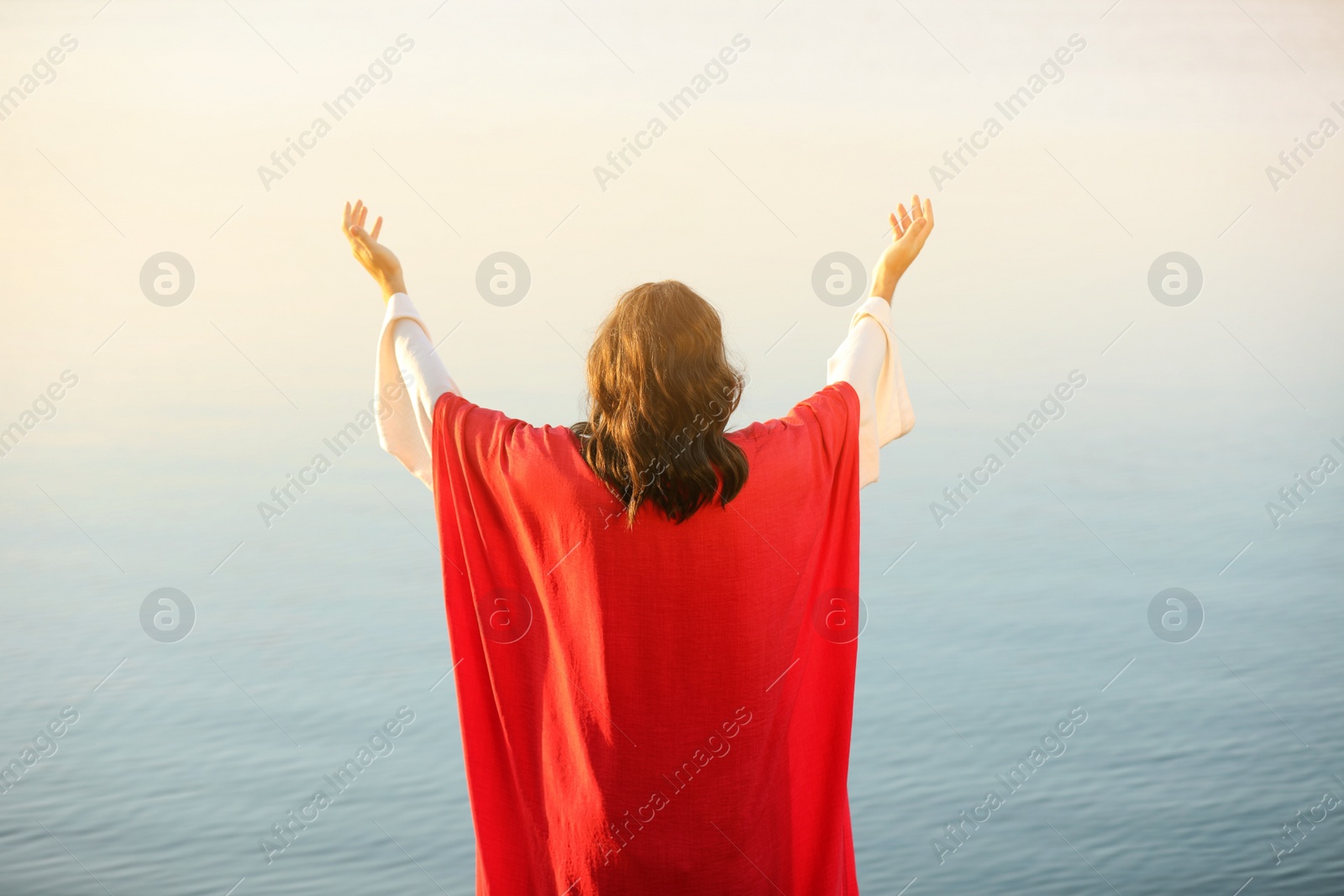 Photo of Jesus Christ raising hands near water outdoors, back view