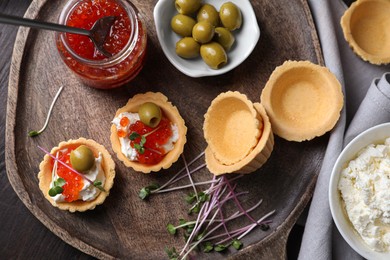 Photo of Delicious tartlets with red caviar and cream cheese served on wooden table, flat lay