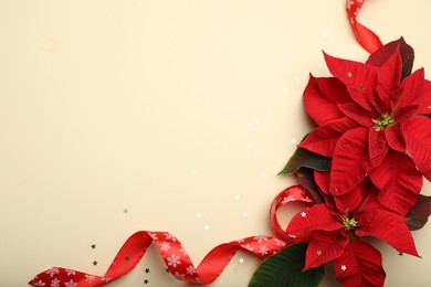 Flat lay composition with poinsettias (traditional Christmas flowers) and ribbon on beige background. Space for text