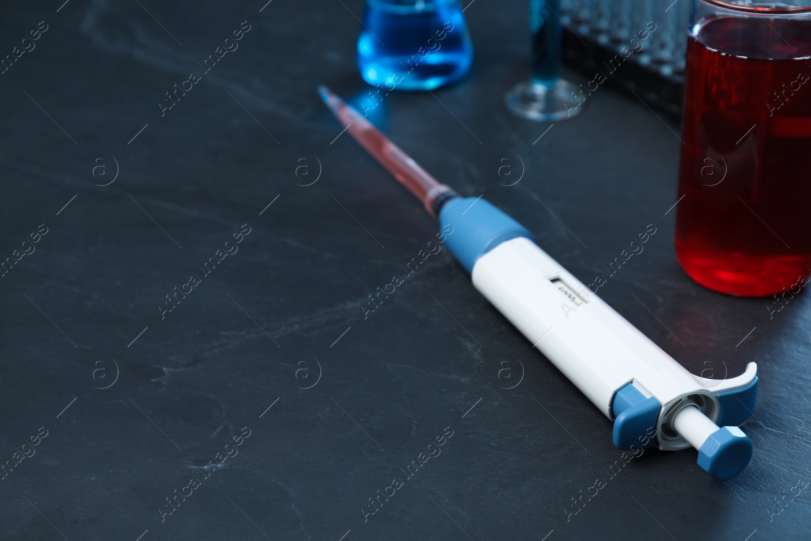 Photo of Laboratory analysis. Micropipette with liquid on black table, closeup. Space for text