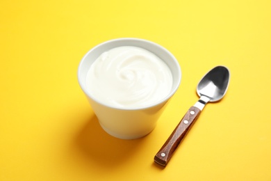 Bowl with creamy yogurt and spoon on color background