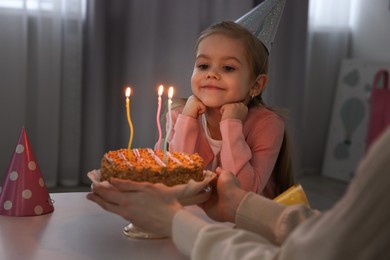 Birthday celebration. Mother holding tasty cake with burning candles near her daughter indoors