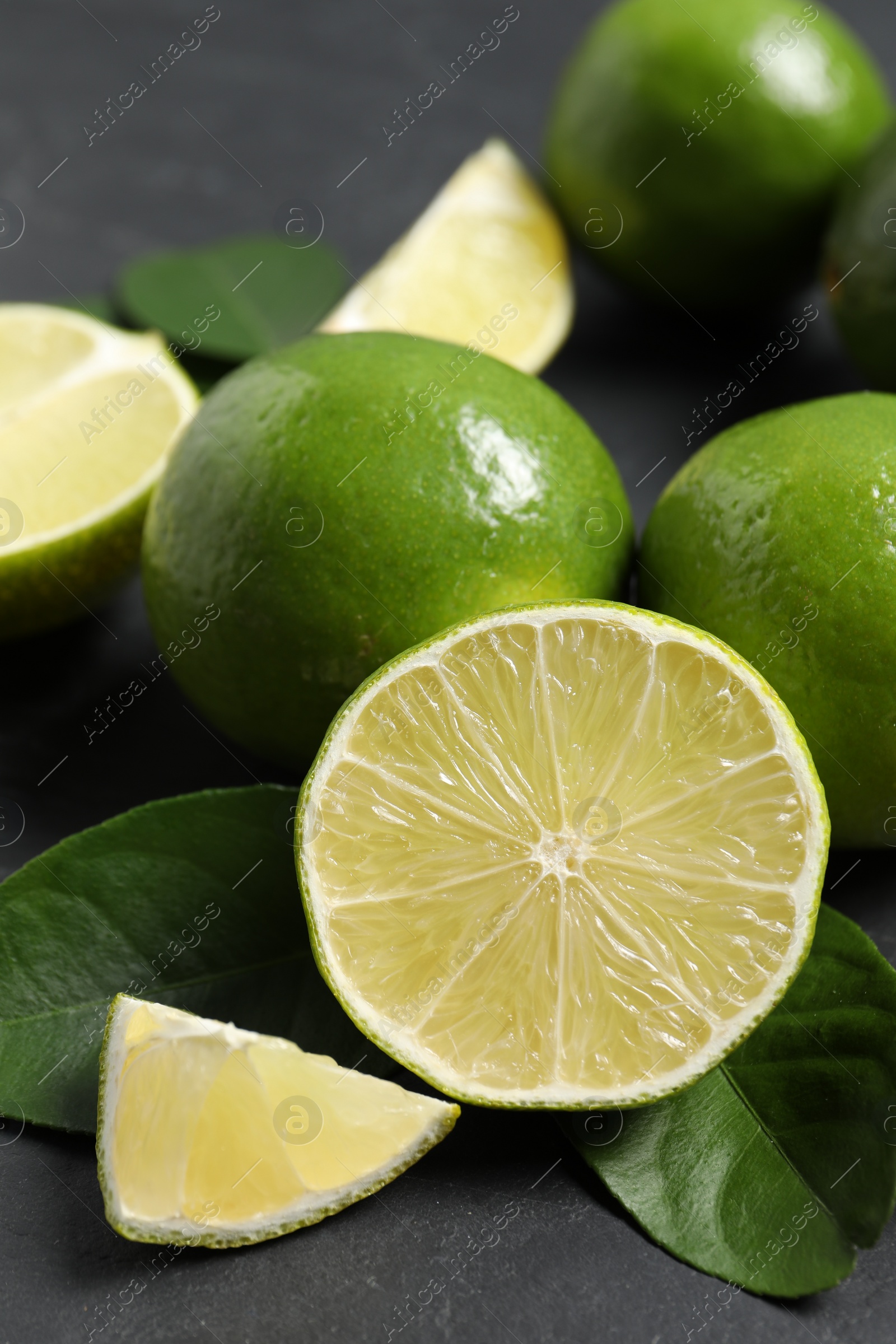 Photo of Fresh ripe limes and leaves on black table, closeup