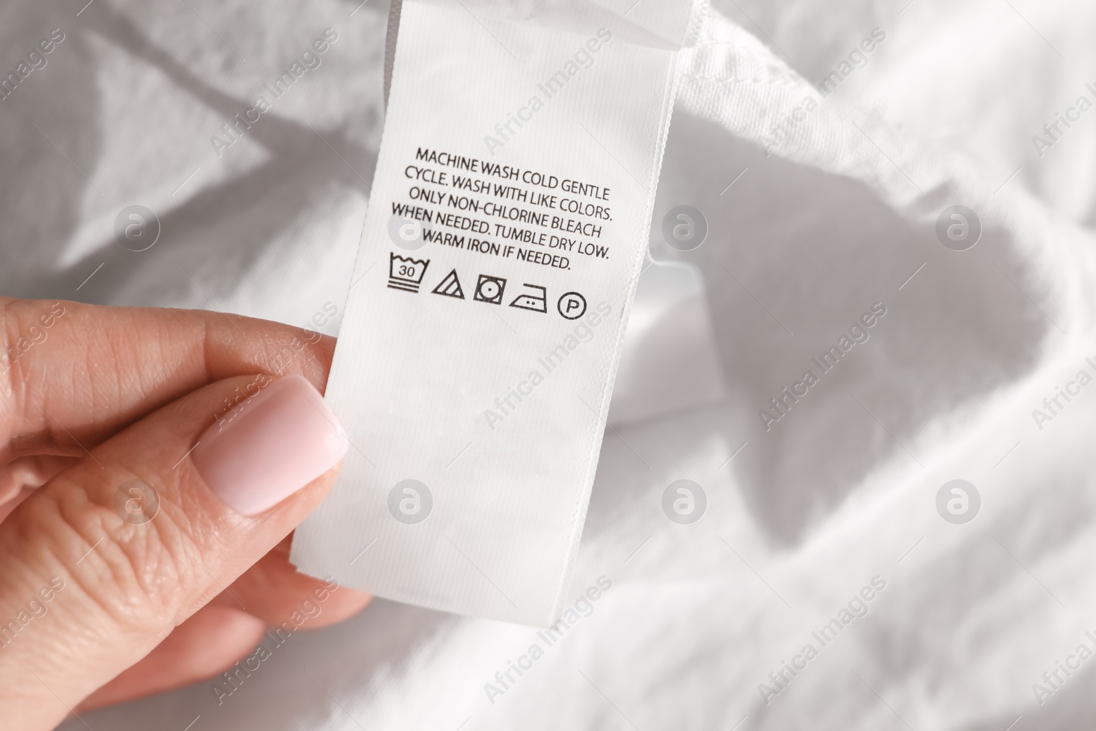 Photo of Woman holding clothing label in different languages on white garment, closeup