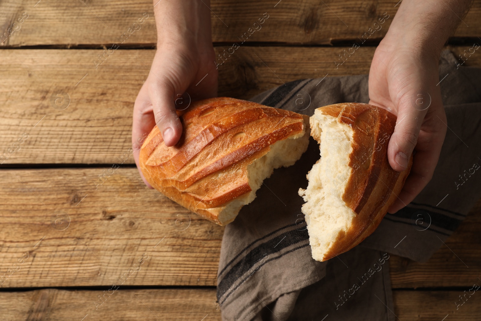 Photo of Man breaking loaf of fresh bread at wooden table, top view