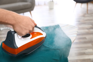 Photo of Man ironing clothes on board at home, closeup