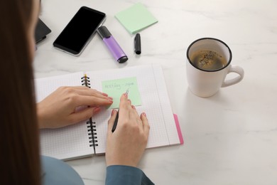 Photo of Woman writing on sticky note at white marble table, closeup