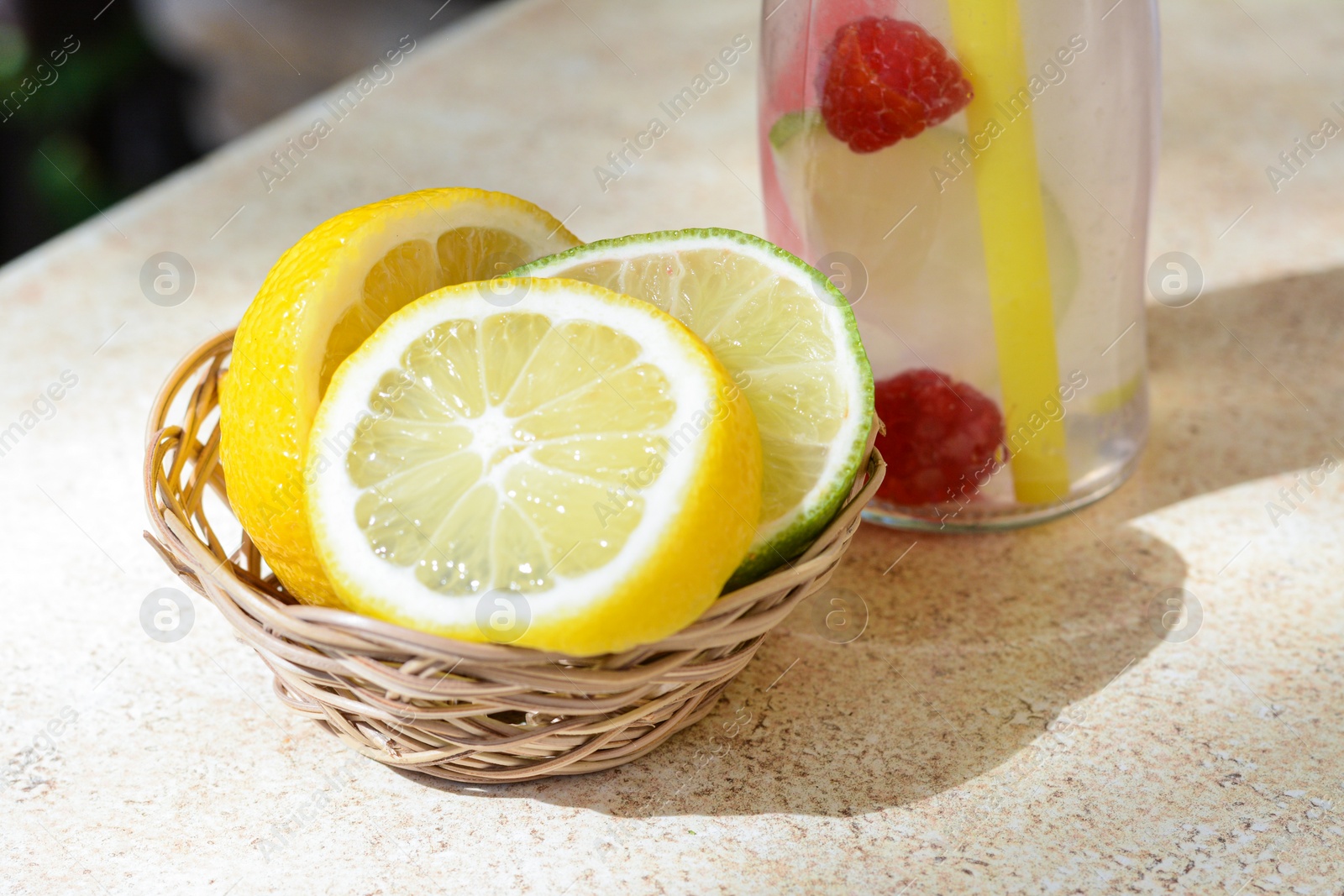 Photo of Citrus fruits and refreshing tasty lemonade served in glass bottle on beige table