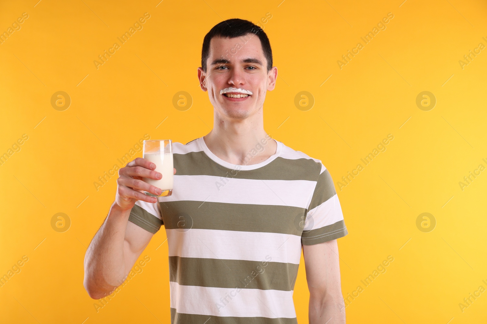 Photo of Happy man with milk mustache holding glass of tasty dairy drink on orange background