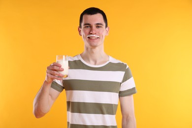 Happy man with milk mustache holding glass of tasty dairy drink on orange background