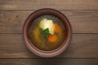 Delicious chicken bouillon with carrot and parsley in bowl on wooden table, top view