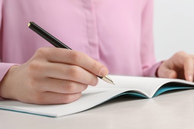 Photo of Woman with pen and notepad at white wooden table, closeup