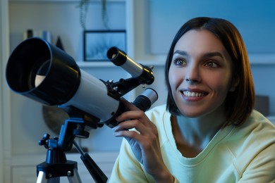 Photo of Beautiful young woman looking at stars through telescope in room