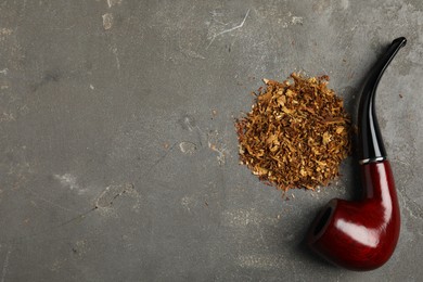 Photo of Pile of tobacco and smoking pipe on grey table, flat lay. Space for text