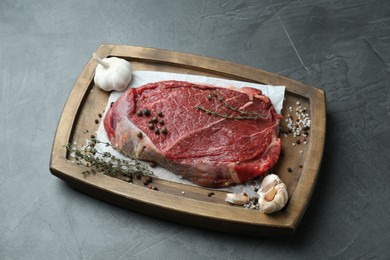 Wooden tray with piece of raw meat, garlic and thyme on grey table