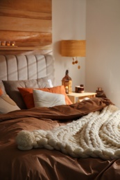 Photo of Bed with cozy knitted blanket and cushions indoors. Interior design