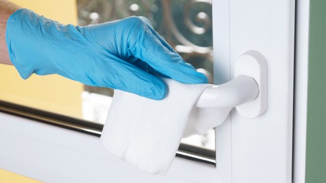 Photo of Man in latex gloves cleaning window handle with wet wipe indoors, closeup. Protective measures