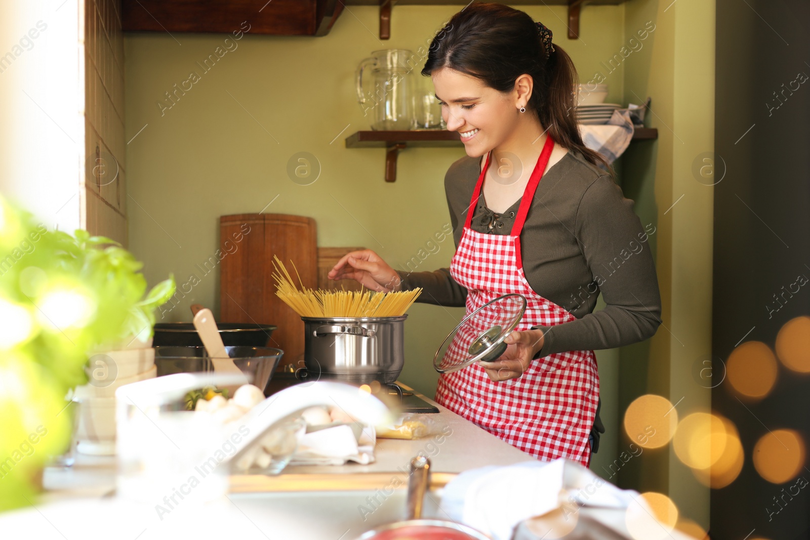 Photo of Young woman cooking spaghetti on stove in kitchen