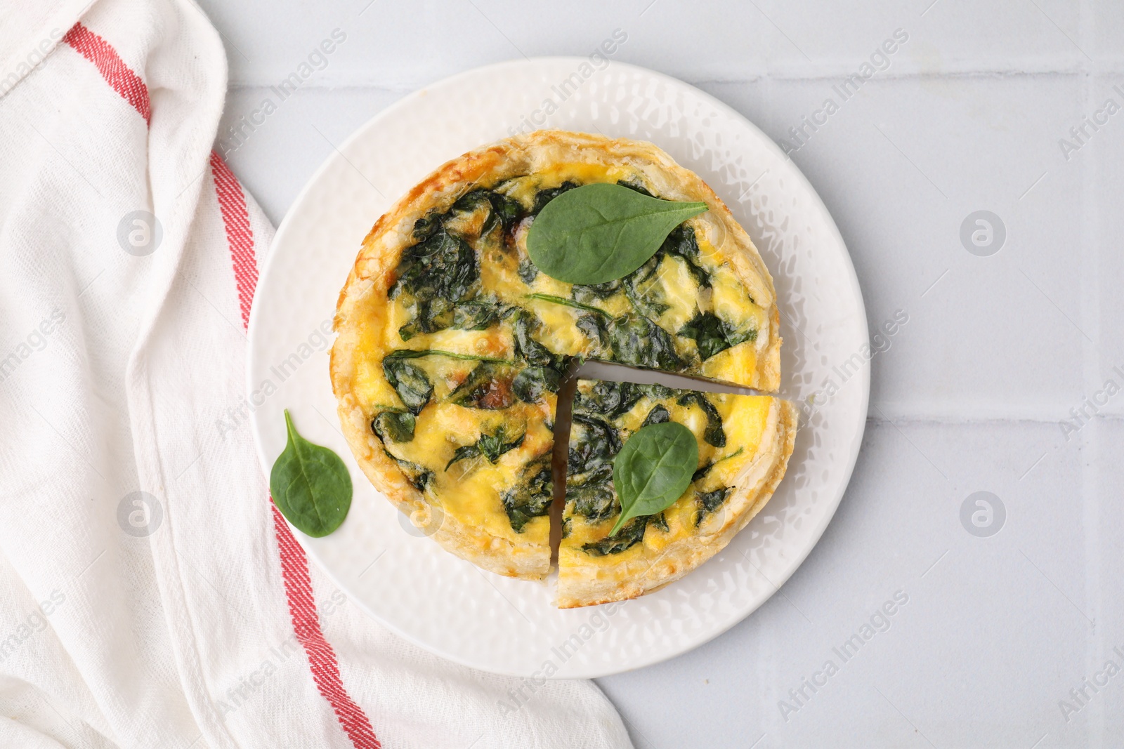 Photo of Delicious pie with spinach on white tiled table, top view