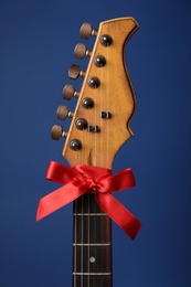Photo of Guitar with red bow on blue background. Christmas music concept
