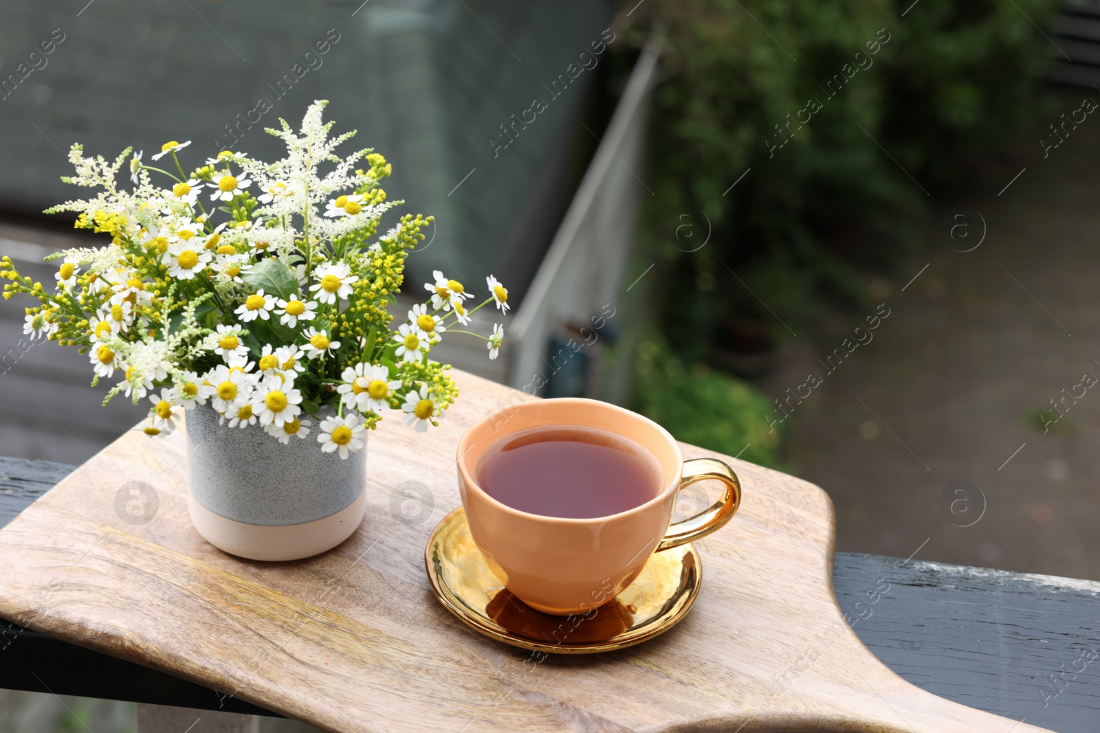 Photo of Cup of delicious chamomile tea and fresh flowers outdoors. Space for text