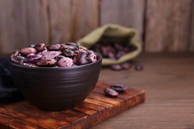 Photo of Bowl with dry kidney beans on wooden table, closeup. Space for text