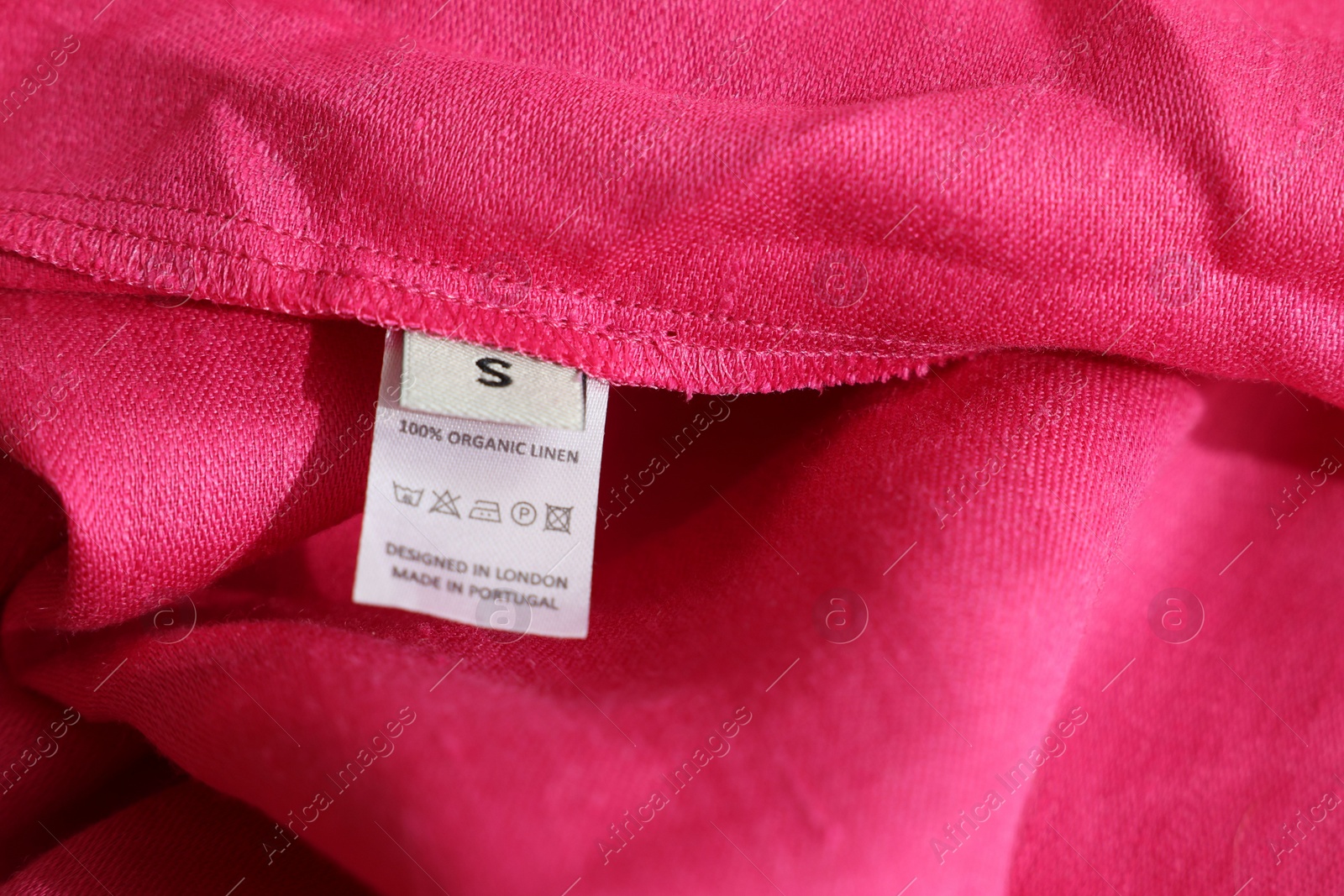 Photo of Clothing label in different languages on pink garment, closeup