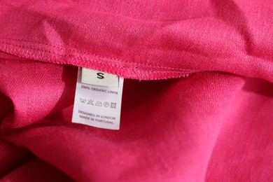 Clothing label in different languages on pink garment, closeup